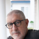 Headshot of a man with close cut grey hair and beard, wearing black glasses and a grey t-shirt.